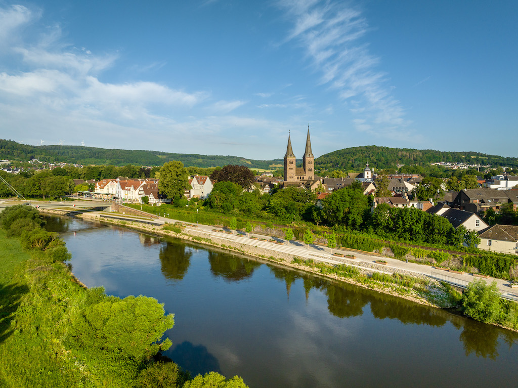 Felsenformation in grüner Landschaft spiegelt sich im See, umgeben von Bäumen bei Sonnenuntergang.